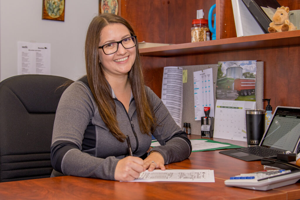 MASC staff seated at an office desk writing on a form, with a laptop, calendar, and office supplies visible.