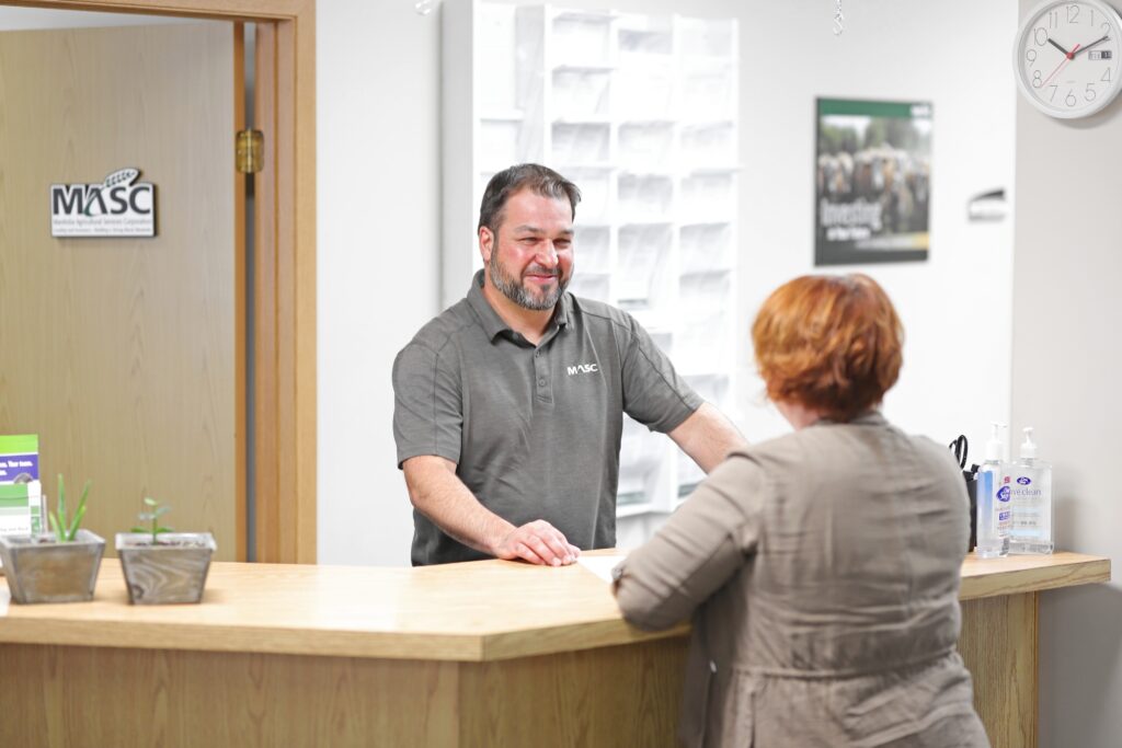 MASC staff standing behind a reception counter speaking with another individual in an office environment.